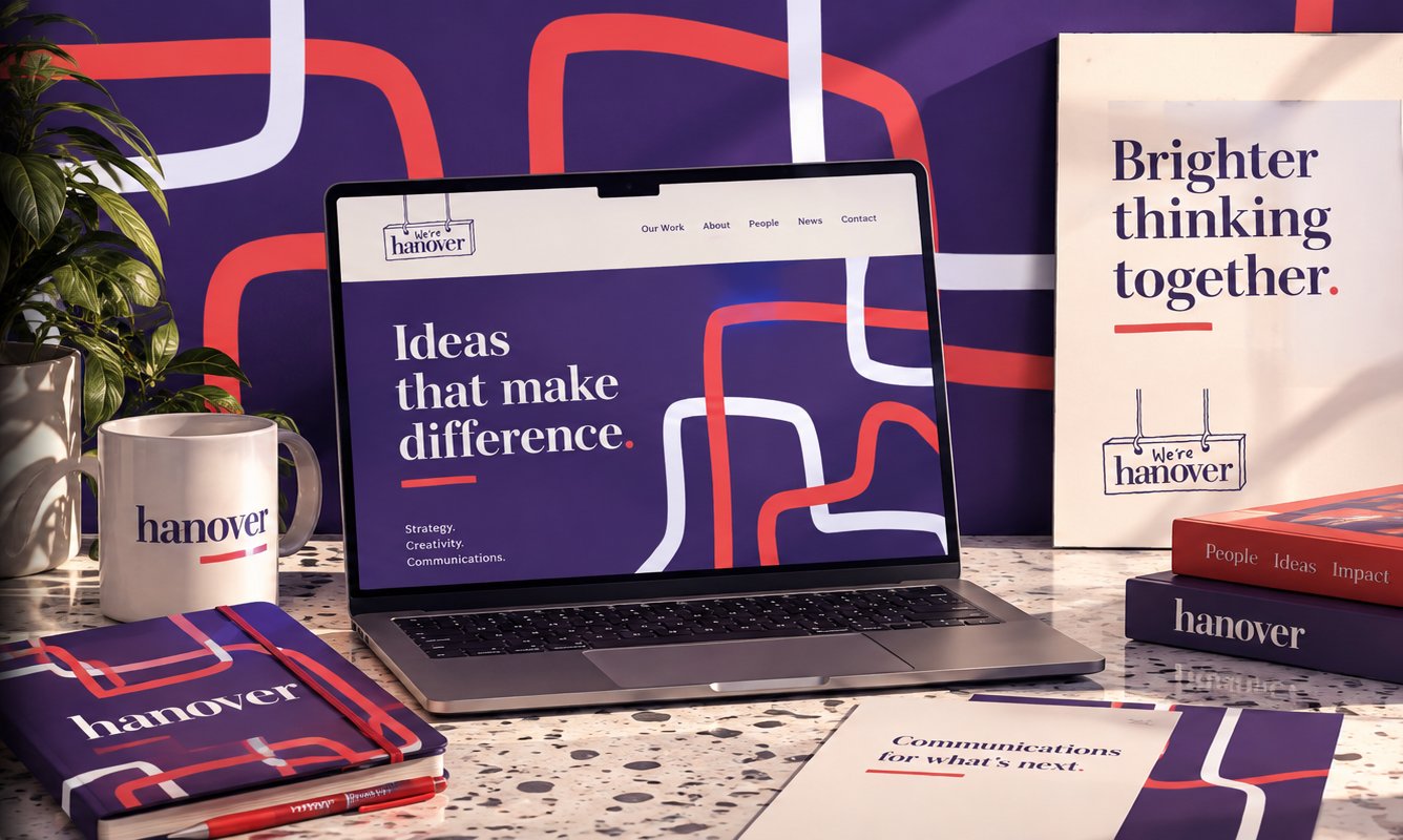 A brand identity flat-lay for Hanover Communications, featuring a laptop displaying the agency's website, alongside branded notebooks, a mug and stationery in a purple, red and white pattern design.