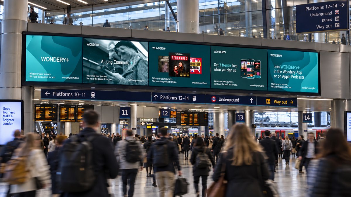 A row of Wondery+ digital screens above the concourse at a London Underground station, running podcast ads for British Scandal, Redhanded and the Wondery+ app.